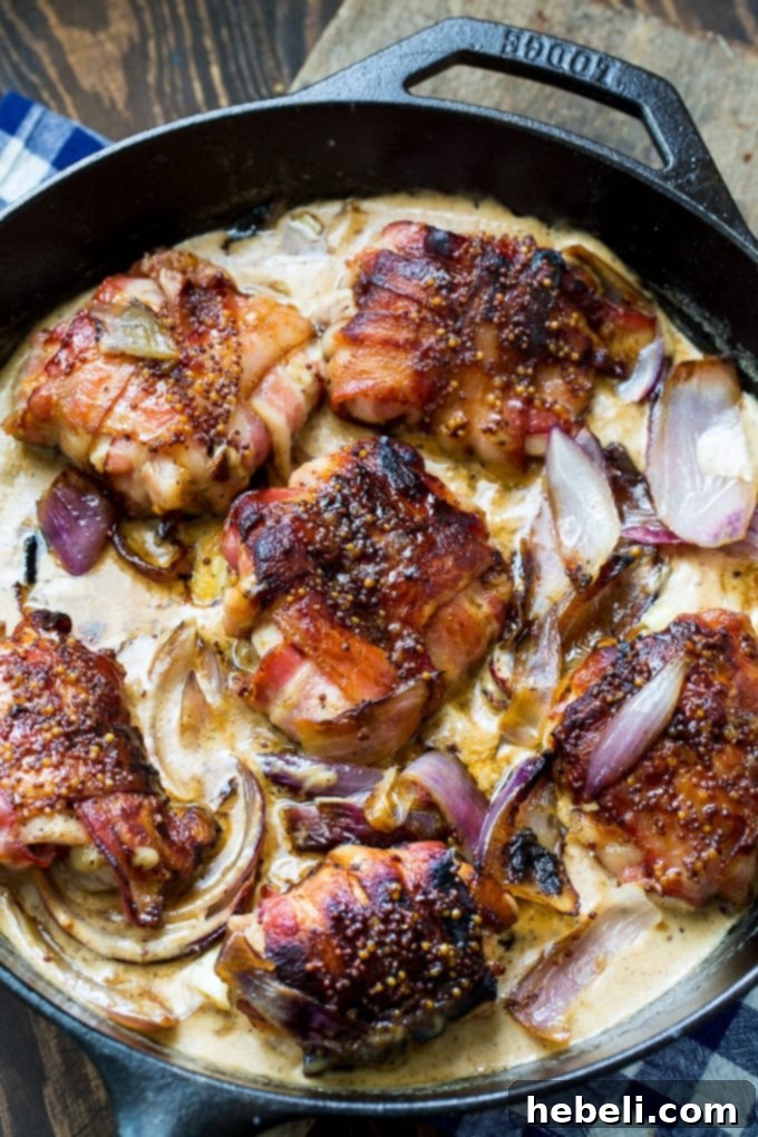 Close-up of a Bacon Wrapped Chicken Thigh being seared in a cast iron skillet with red onions, showing golden crust