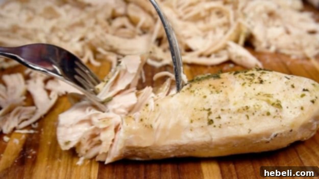 Addictive Instant Pot Chicken 5 Shredding the perfectly cooked chicken breasts on a cutting board using two forks.