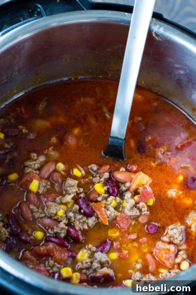 Close-up of a bubbling pot of Instant Pot Taco Soup, showing seasoned ground beef, beans, and corn, topped with melting shredded cheese