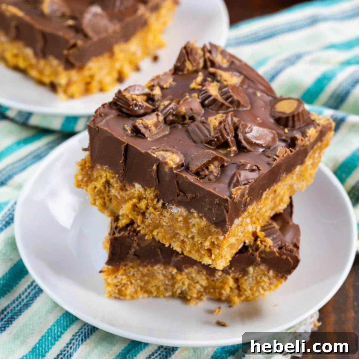 No-Bake Chocolate Peanut Butter Crispy Squares 2 Two decadently rich Chocolate Peanut Butter Rice Krispie Treats on a pristine white plate, showcasing their irresistible layers of crispy cereal, creamy peanut butter, and smooth chocolate topping, sprinkled with mini peanut butter cups.
