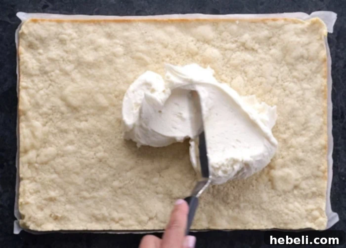 Spreading creamy buttercream frosting over cooled sugar cookie bars