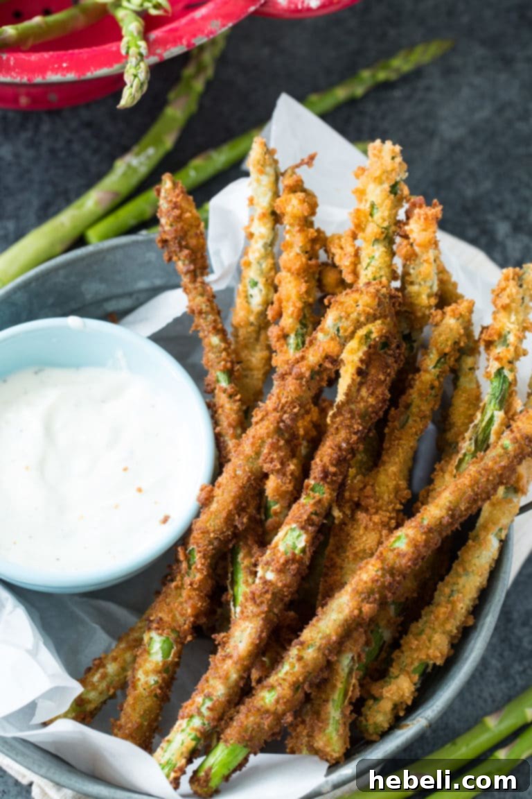 Fresh asparagus spears being coated in a homemade breadcrumb mixture inside a zip-top bag, illustrating the preparation for deep frying.