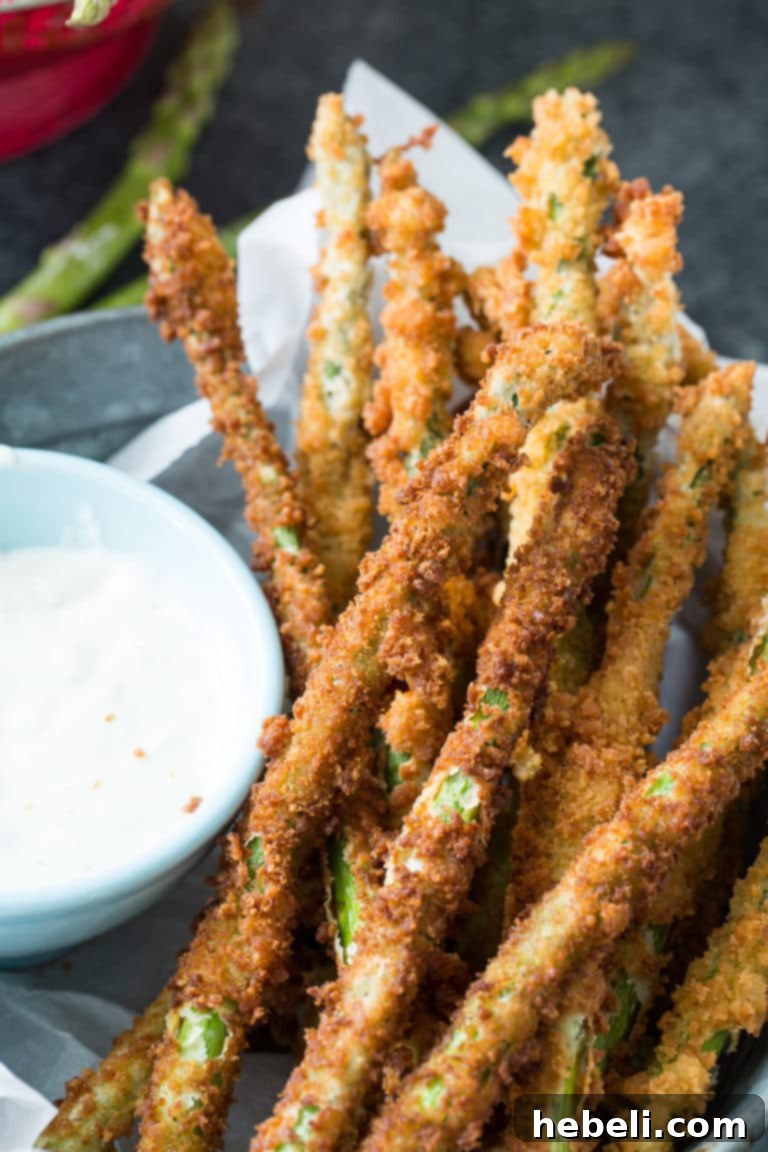 A close-up of crispy fried asparagus spears piled high on a plate, showcasing their golden-brown, textured coating. A perfect appetizer or side dish.