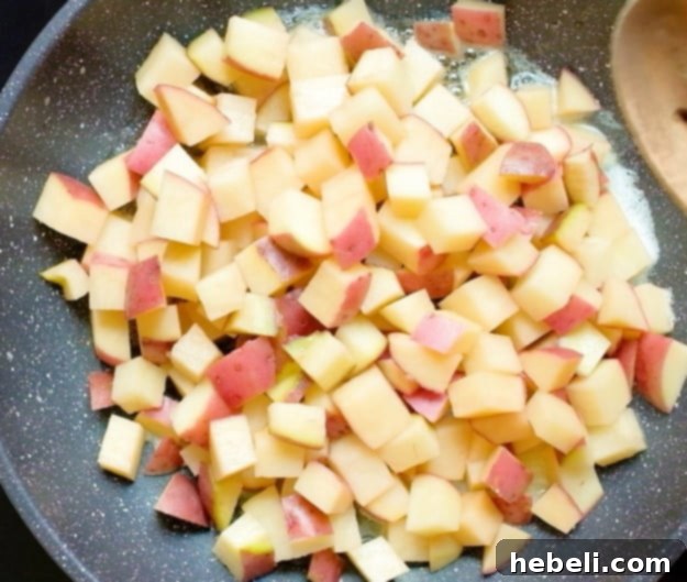 Diced red potatoes sizzling in a skillet with bacon grease and butter, beginning to brown.