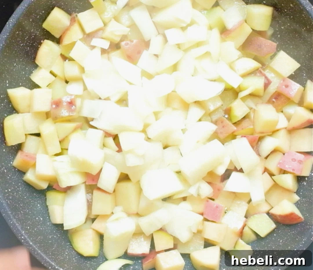 Chopped Vidalia onion being added to the skillet with the cooking potatoes, releasing its aroma.