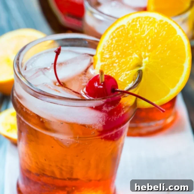 A refreshing Bourbon Amaretto Cocktail garnished with an orange slice and maraschino cherries