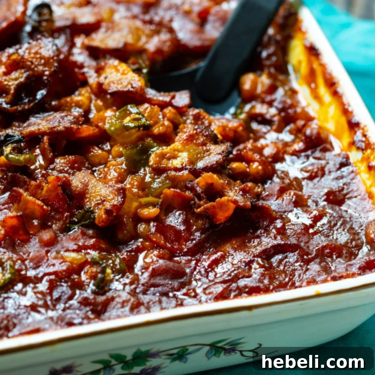 Spicy Bacon Baked Beans getting scooped out of baking dish.