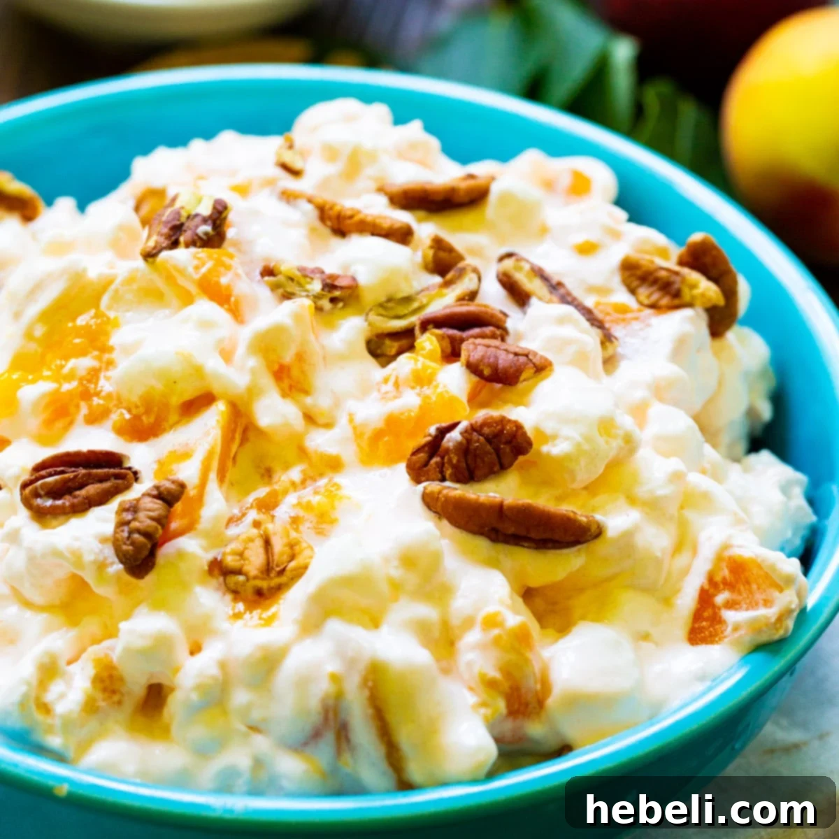 Golden Peach Ambrosia 2 A vibrant blue bowl filled with creamy Millionaire Peach Salad, garnished with a maraschino cherry and ready to serve.