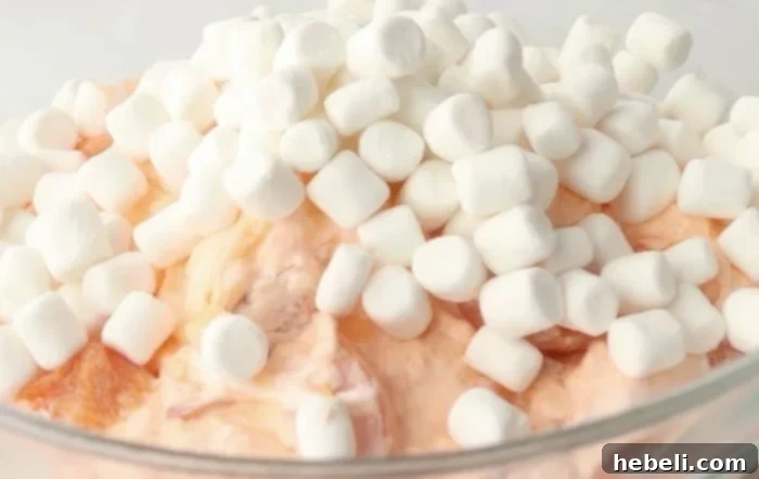 Golden Peach Ambrosia 7 Mini marshmallows being carefully stirred into the peach salad mixture, ensuring even distribution.