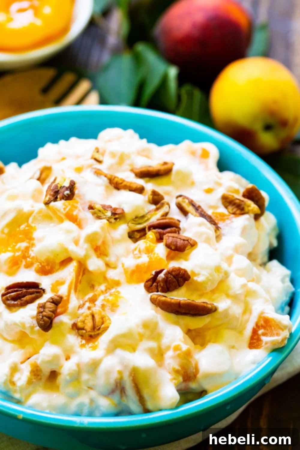 Golden Peach Ambrosia 9 A bowl of Peach Fluff beautifully presented, with fresh peaches artfully arranged in the background, highlighting the key ingredient.
