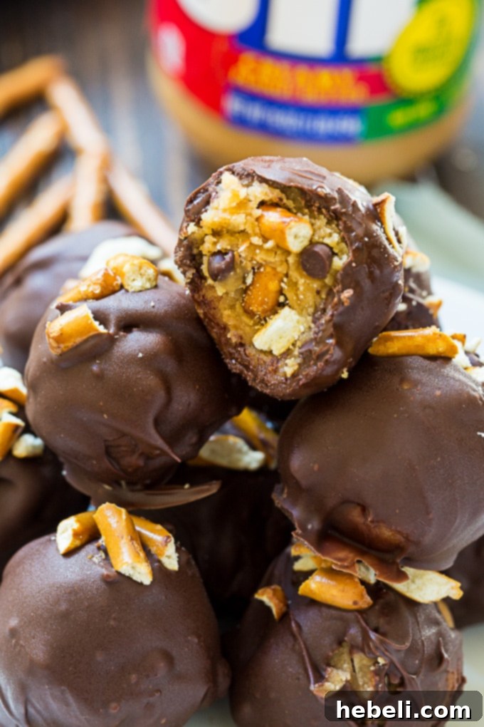 A tray of freshly dipped Peanut Butter Pretzel Truffles, some with extra pretzel crumbs, cooling on parchment paper.