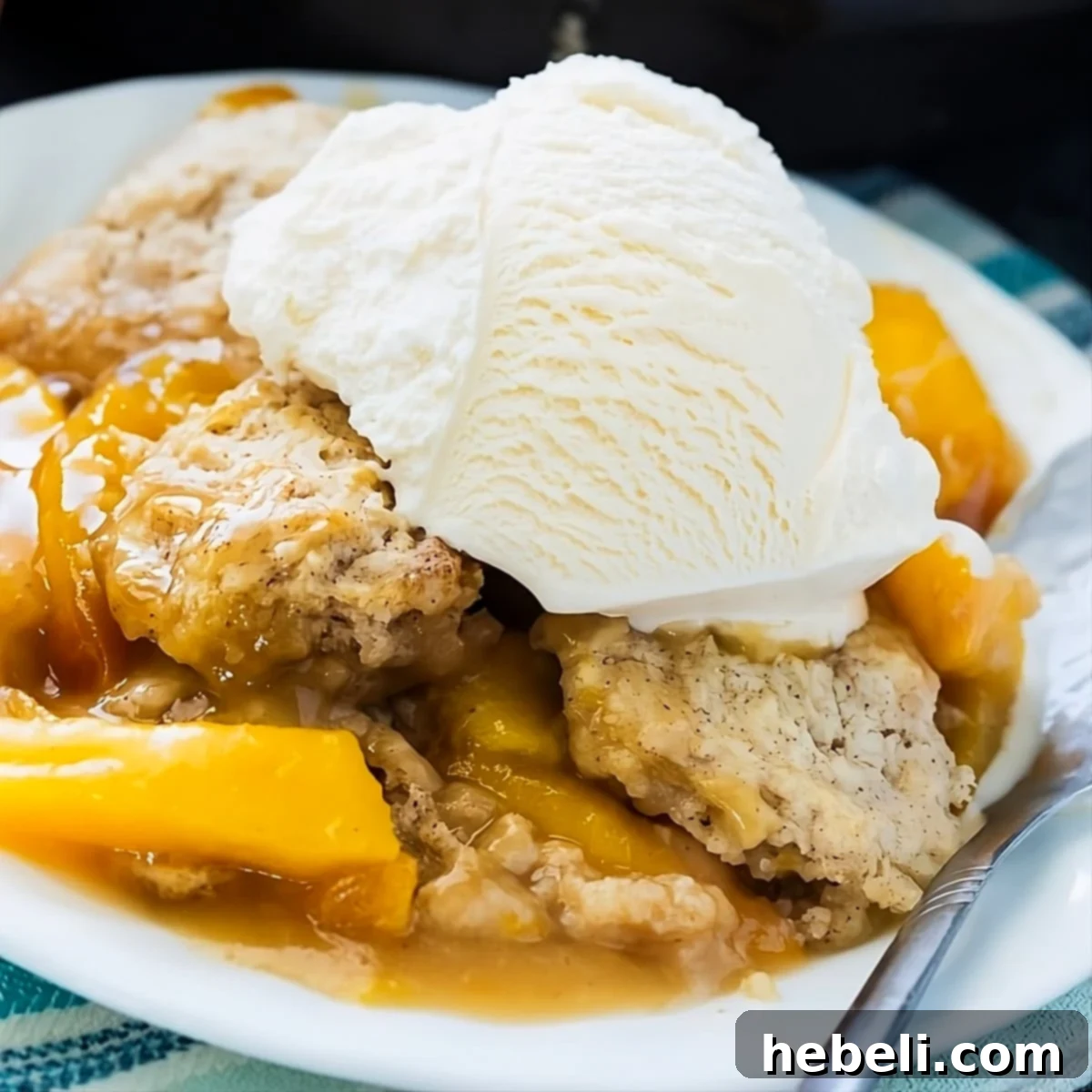 A close-up of Skillet Bourbon Peach Cobbler, richly golden, bubbling with peaches and topped with a melting scoop of vanilla ice cream, ready to be enjoyed.