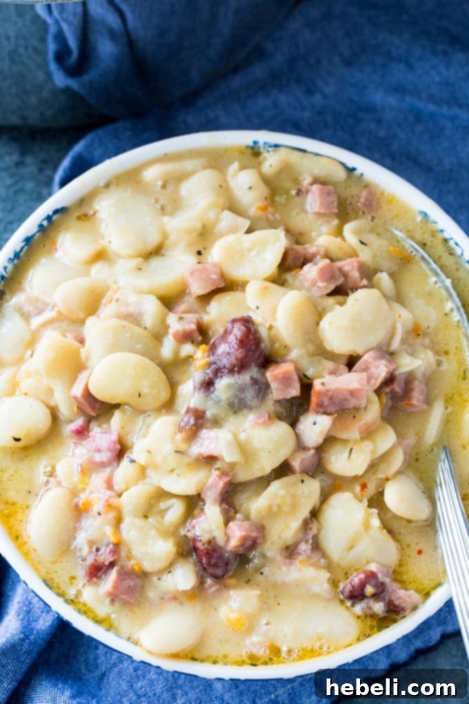 A close-up of a bowl of creamy butter beans, rich with pieces of smoked ham and a vibrant, thick sauce, inviting diners to savor its flavor.