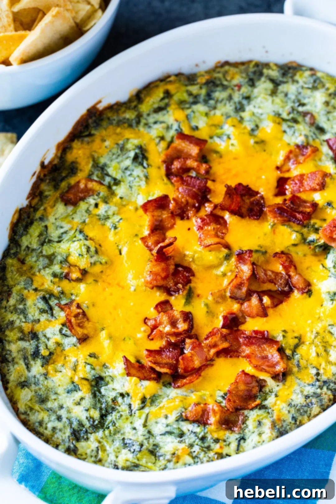 Close-up of baked Warm Turnip Green Dip generously topped with melted cheddar cheese and crispy bacon crumbles.