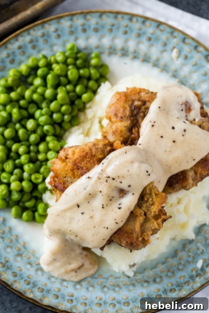 Close-up of a Chicken Fried Hamburger patty with creamy white gravy.