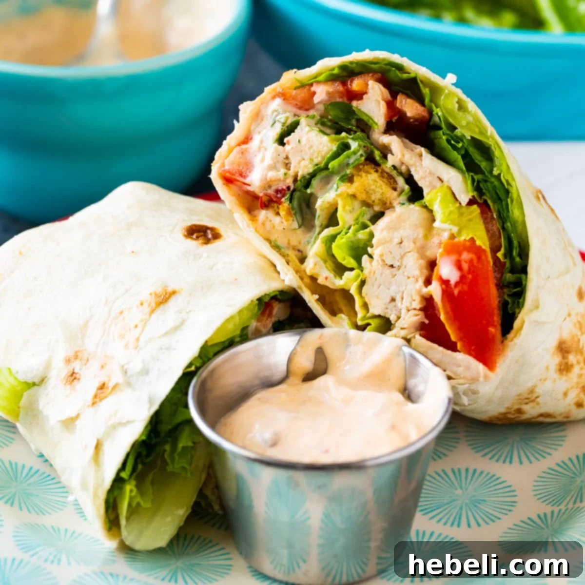 A Spicy Chicken Caesar Salad Wrap, cut in half, showcasing its vibrant filling of chicken, lettuce, and creamy dressing on a plate.