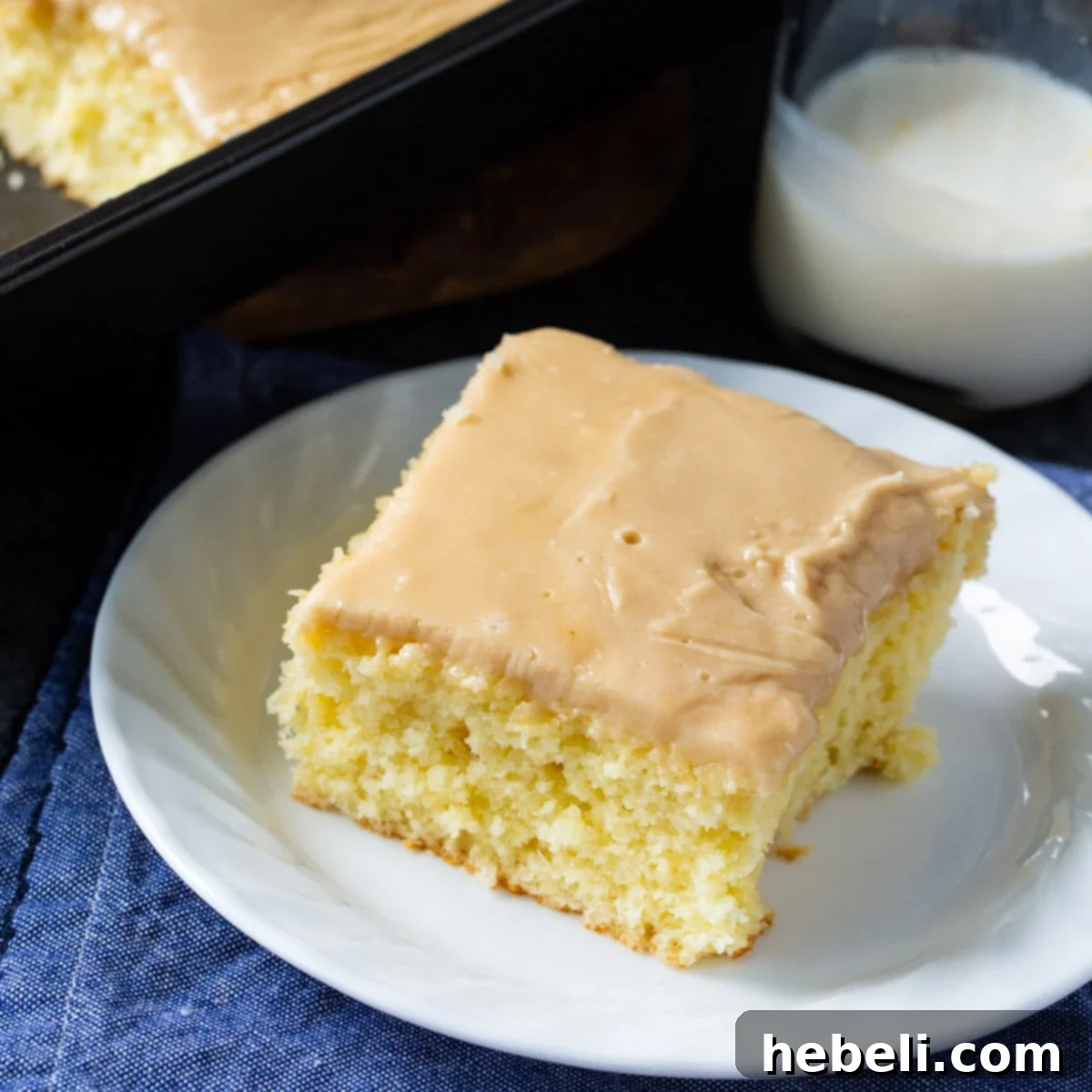 A perfectly sliced piece of Buttermilk Sheet Cake with Caramel Icing on a small white plate, showcasing its moist texture and rich caramel topping.