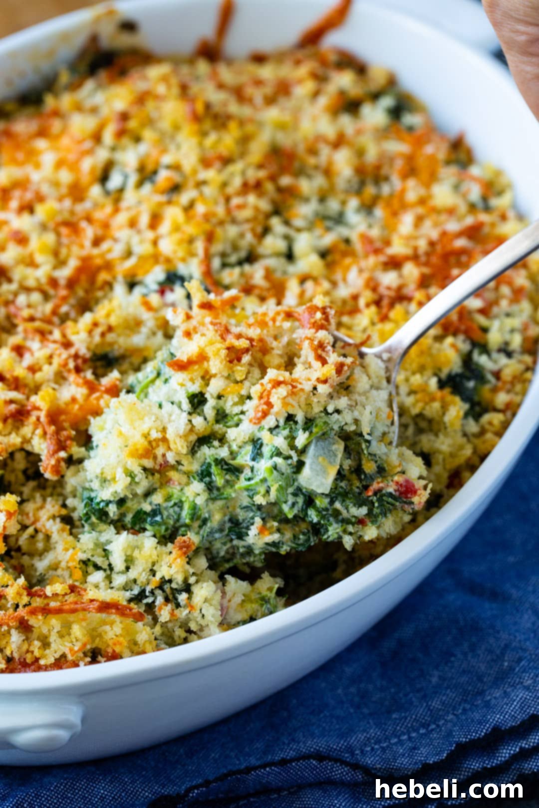 Southern Pimento Cheese Creamed Spinach 3 Close-up of a spoon lifting a rich, cheesy serving of Pimento Cheese Creamed Spinach, highlighting its vibrant green and red hues.