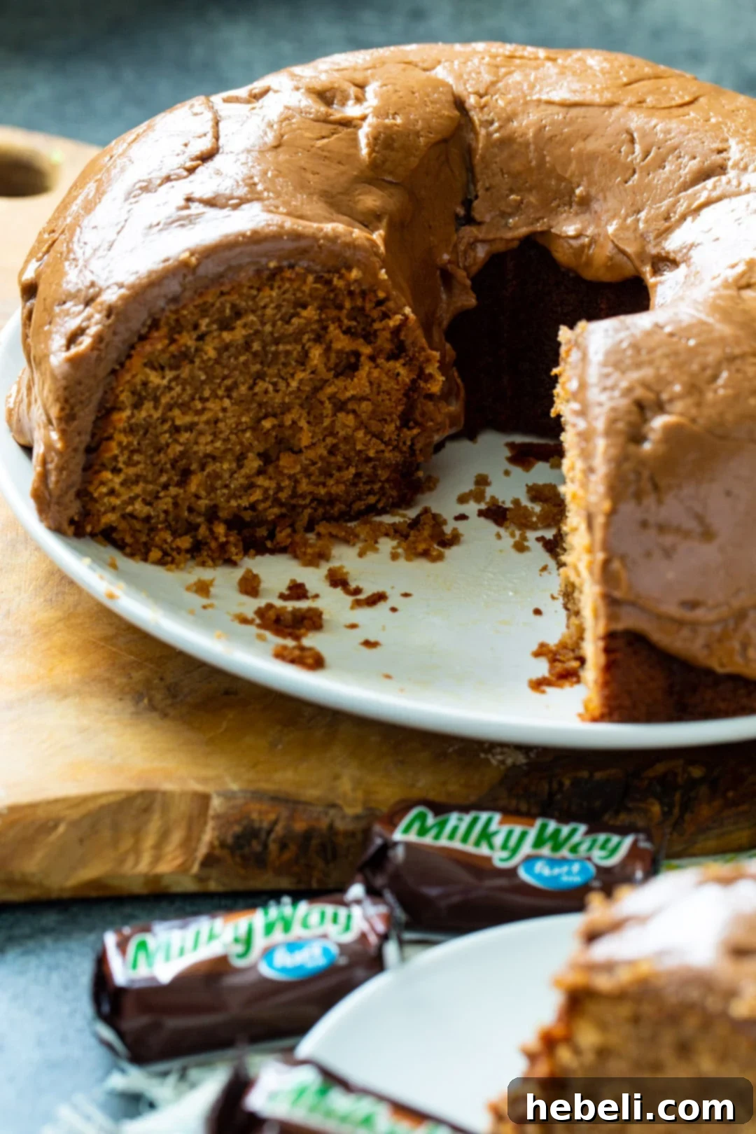 A whole Milky Way Pound Cake with a few slices already cut out, revealing the moist interior and rich frosting, inviting viewers to serve themselves.