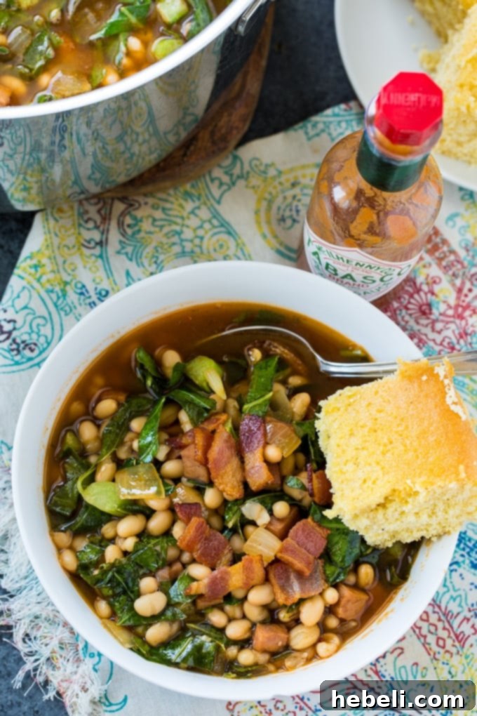 Close-up shot of White Bean and Collard Green Soup simmering gently in a large Dutch oven, showing the vibrant green collards and plump white beans in a rich, reddish-brown broth.