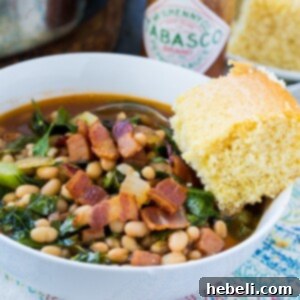 A spoonful of White Bean and Collard Green Soup showing tender greens and beans, served in a bowl with a slice of cornbread.