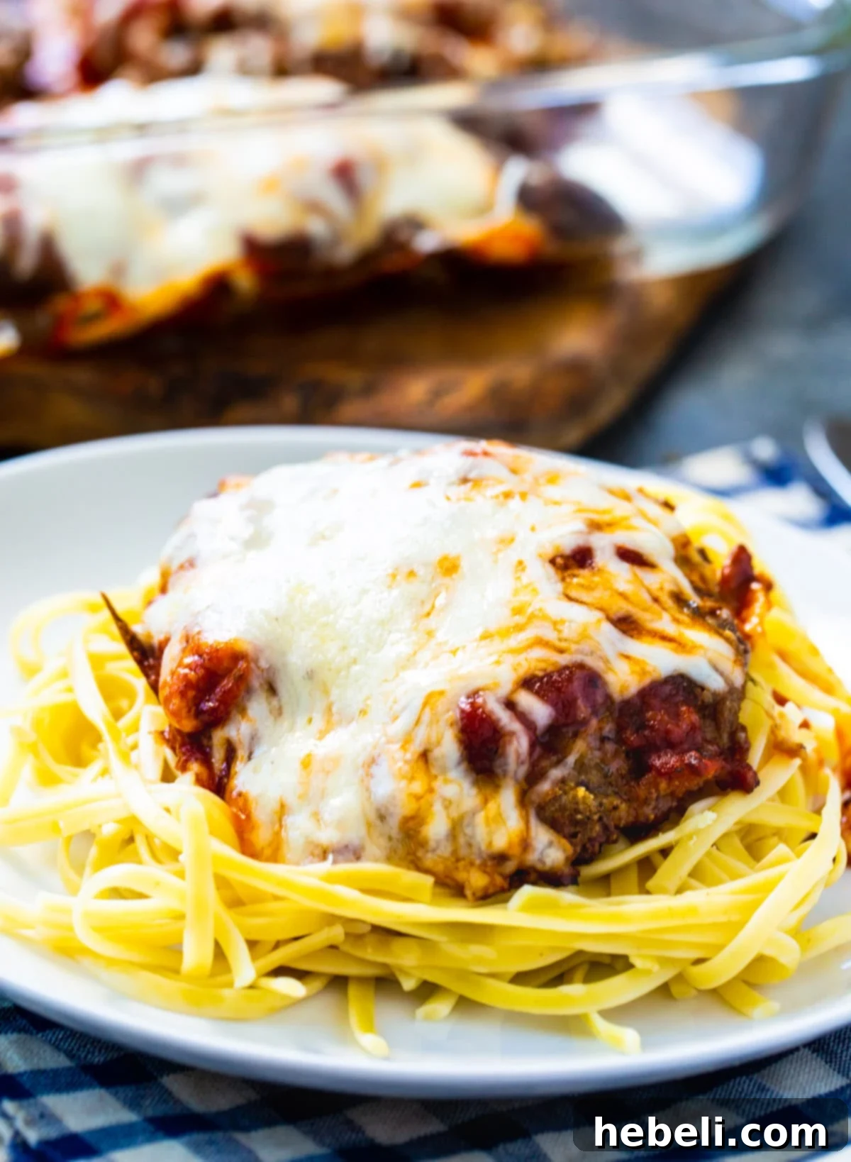 Close-up of a breaded cubed steak covered in melted mozzarella and Parmesan cheese, resting on a bed of spaghetti.