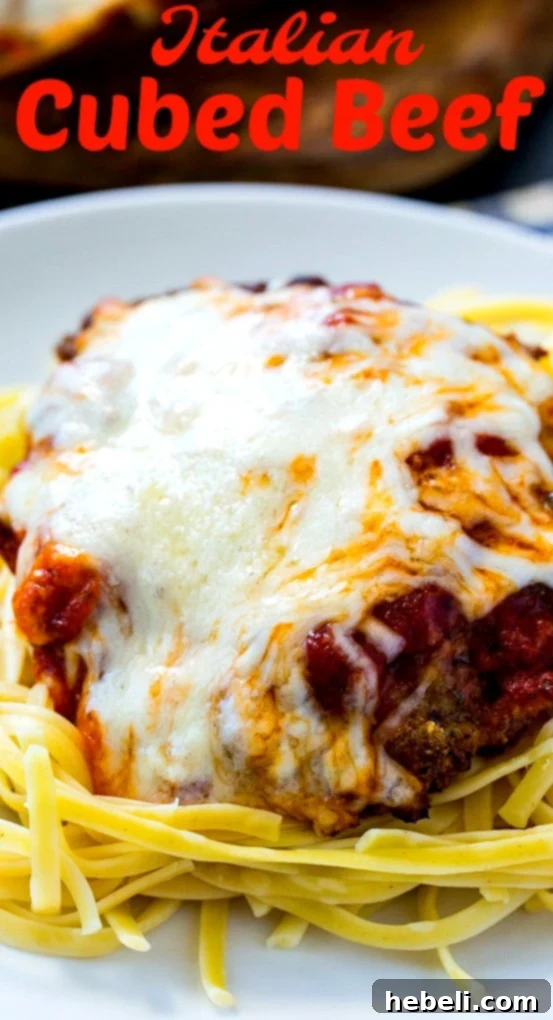 Close-up of Italian Cubed Beef covered with melted cheese and fresh herbs on a bed of spaghetti.
