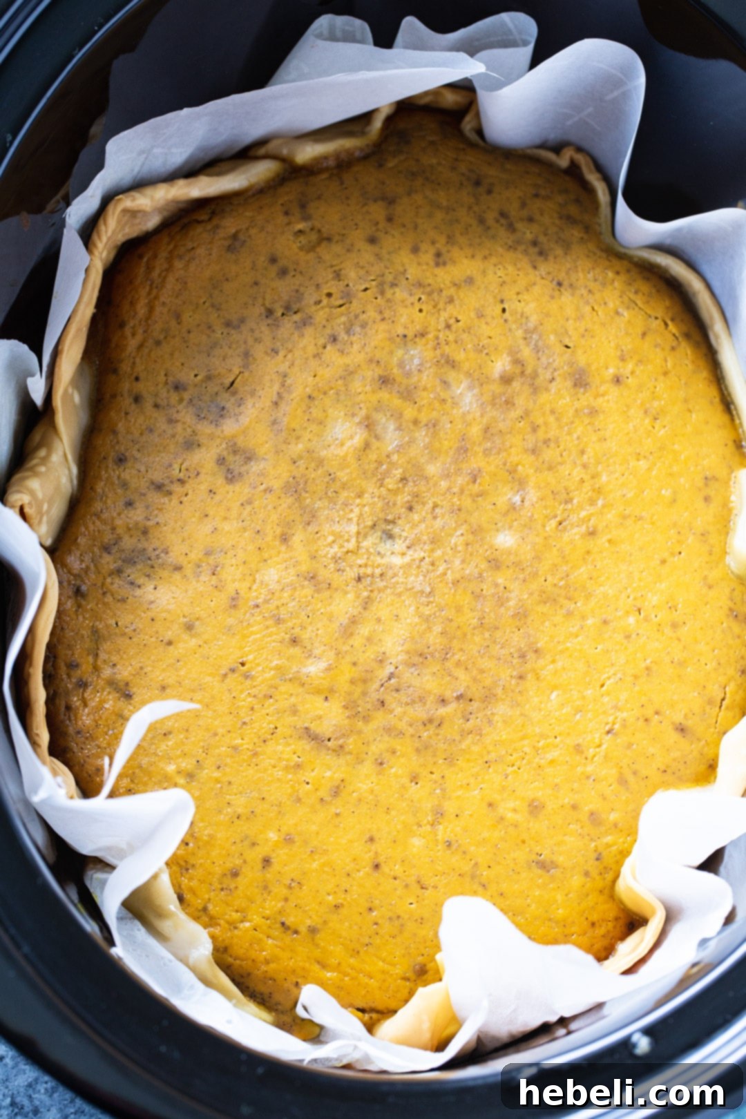 A freshly assembled pumpkin pie, ready for cooking, carefully placed inside a slow cooker liner. The edges of the pie crust are visible, along with the smooth, orange pumpkin filling.
