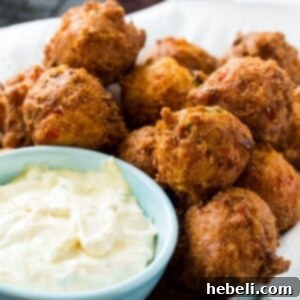 Golden Crab Bites 5 Crab Hush Puppies with a small bowl of Remoulade sauce on the side for dipping.