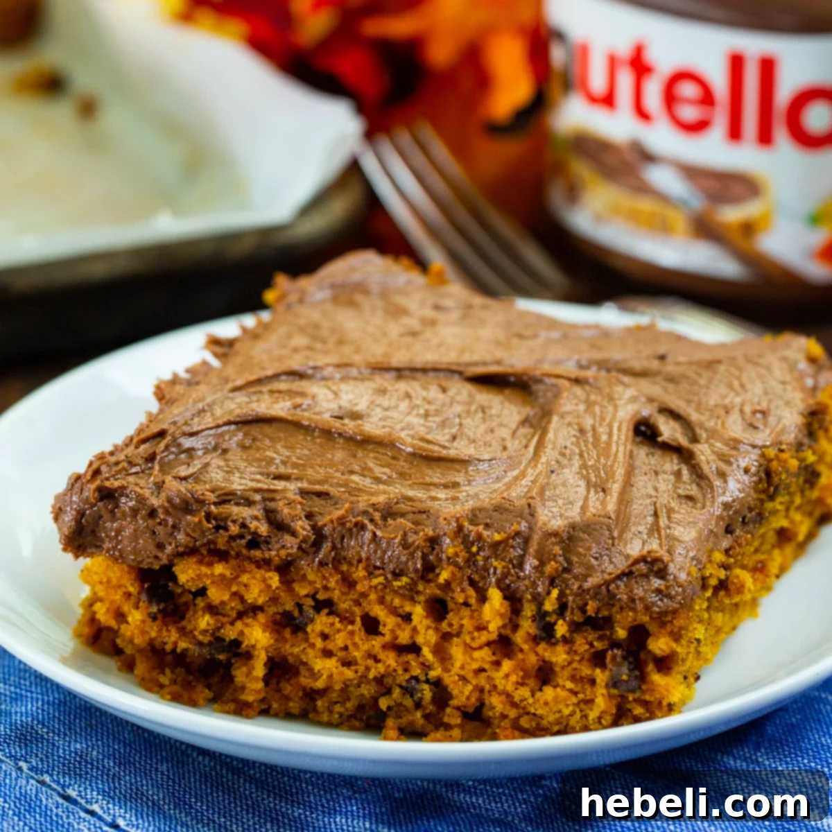 A perfectly sliced piece of Pumpkin Sheet Cake with Nutella Cream Cheese Frosting resting on a white plate, showcasing its moist texture and thick, creamy topping.
