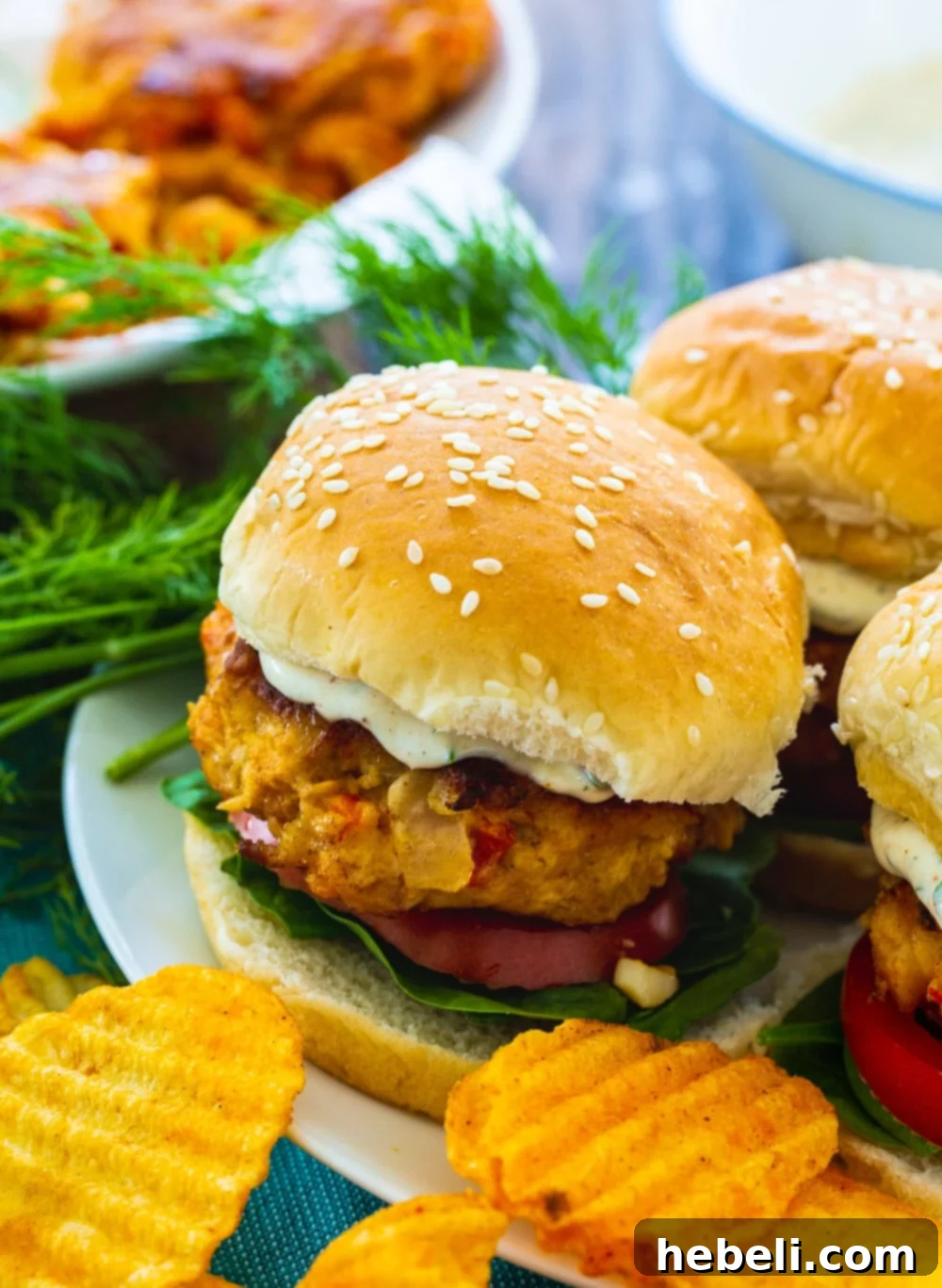 Three Crawfish Burgers arranged beautifully on a plate with fresh greens and a side of chips.