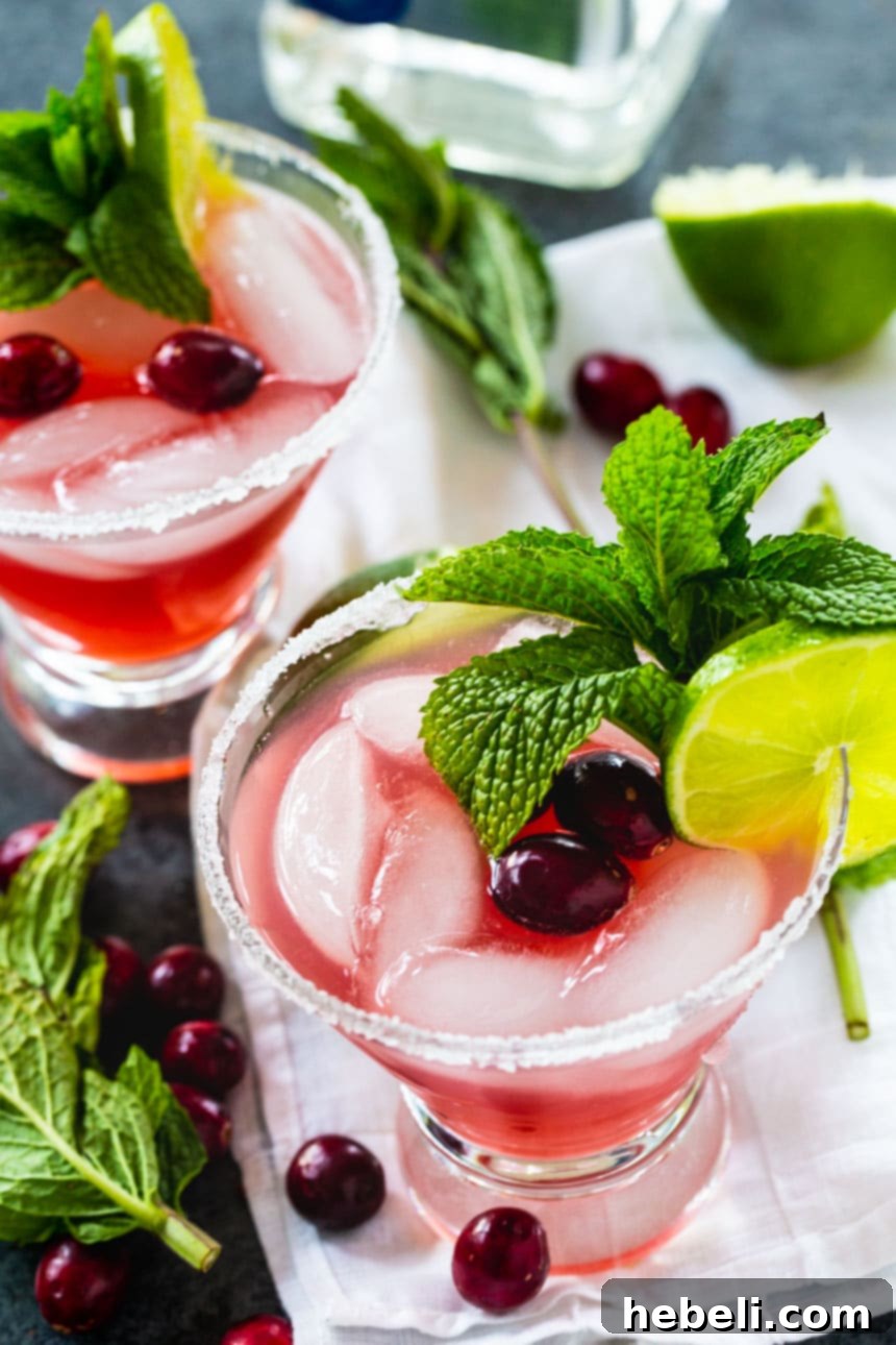 Jingle Juice Margaritas 2 Two vibrant Christmas Margaritas adorned with fresh mint sprigs and cranberries, showcasing a festive holiday cocktail.