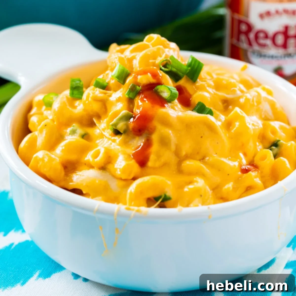 A serving of creamy and spicy Buffalo Chicken Mac and Cheese in a white bowl, garnished with blue cheese and green onions.