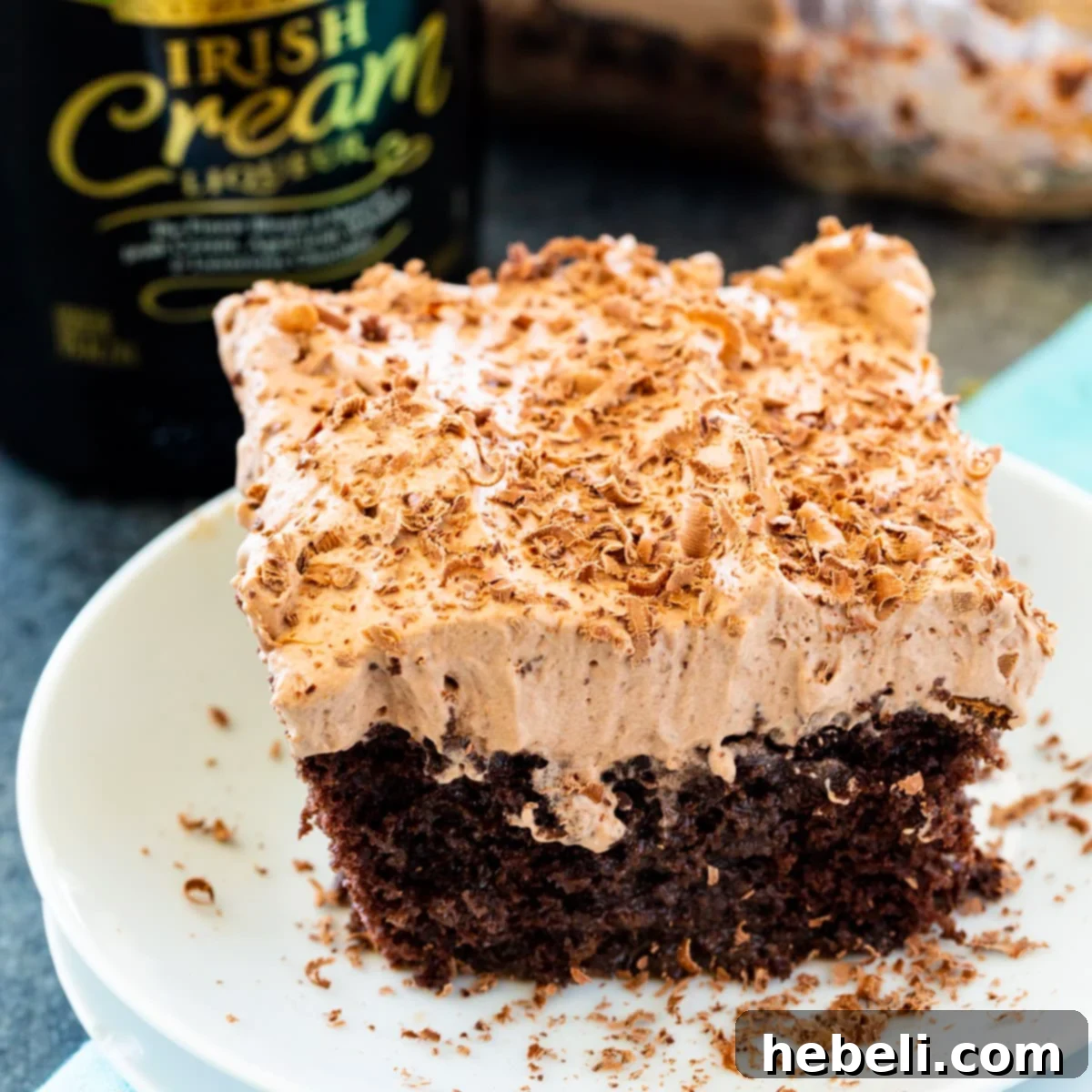 A slice of Irish Cream Poke Cake on a white plate, showcasing its moist texture and creamy topping, garnished with grated chocolate.
