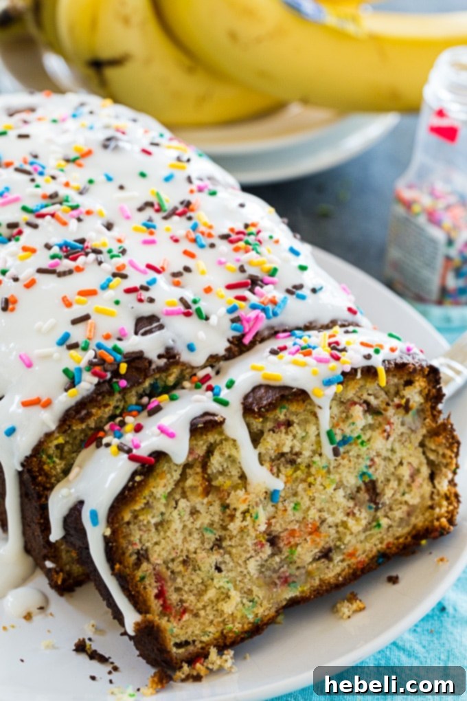 A beautifully glazed Funfetti Banana Bread, adorned with colorful sprinkles, sitting on a wooden cutting board.