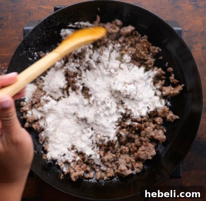 Sausage Gravy Stuffed Biscuit Cups 3 Image showing flour being sprinkled over browned sausage in a skillet, creating the base for gravy