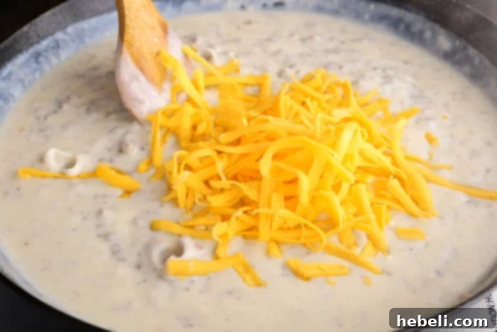 Sausage Gravy Stuffed Biscuit Cups 5 Image showing shredded cheddar cheese being stirred into the thick sausage gravy