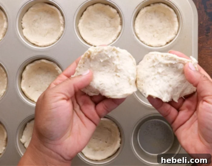 Sausage Gravy Stuffed Biscuit Cups 6 Image showing biscuit dough being pressed into a muffin tin to form cups