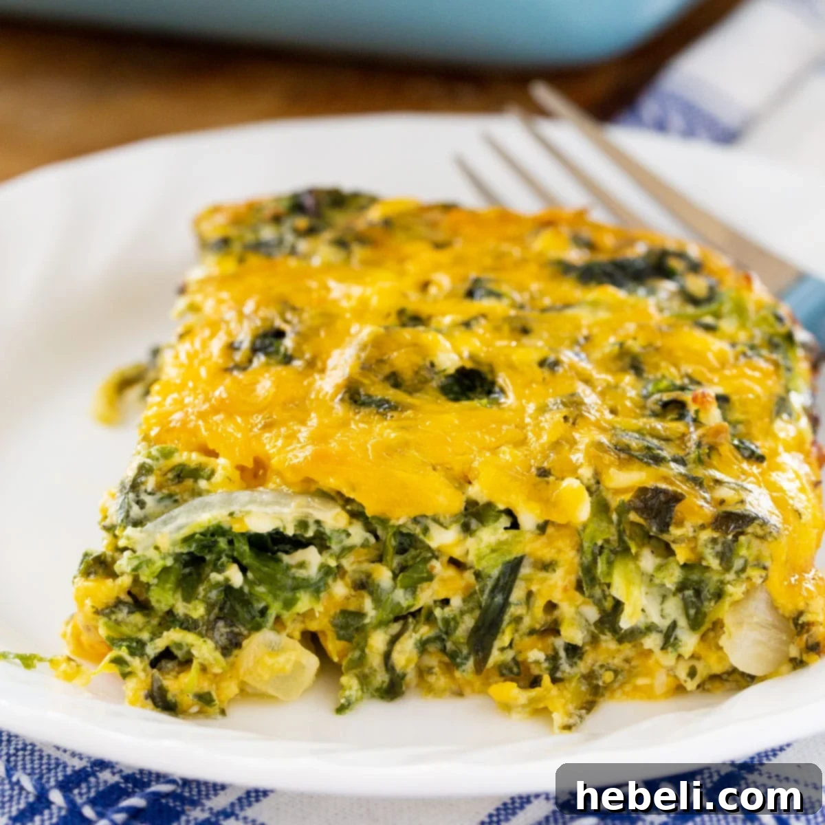 Creamy Spinach and Cheese Bake 2 Slice of creamy spinach and cheese casserole on a white plate with a fork, ready to be enjoyed.