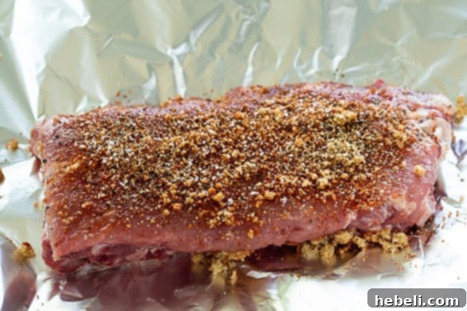 Raw baby back ribs generously coated with a savory dry rub, ready for baking.