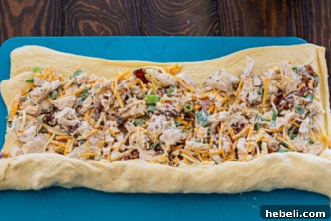 Chicken, bacon, cheese, and Ranch filling being spread evenly over a sheet of crescent roll dough.