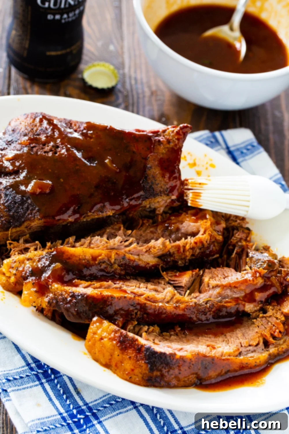 A large serving platter showcasing perfectly sliced slow cooker brisket, accompanied by a small bowl of savory sauce.