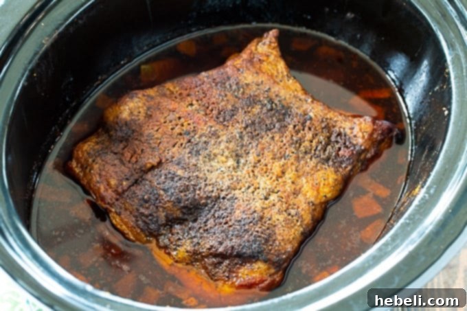 A 4-pound beef brisket seasoned and ready to be slow-cooked in a 6-quart crock pot, alongside chopped onions.