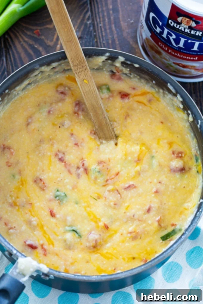 Creamy Tomato Cheese Grits 3 A pot bubbling with creamy Cheesy Tomato Grits on the stovetop, stirred with a wooden spoon.