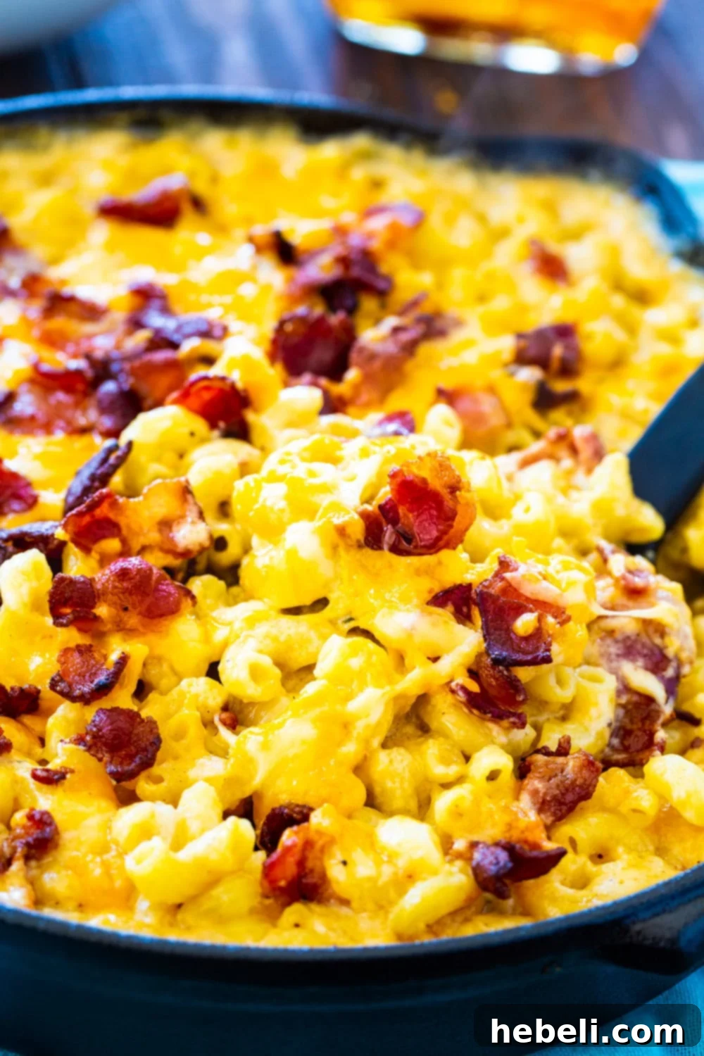 Close-up shot of the creamy Bourbon and Bacon Mac and Cheese, garnished with extra crispy bacon, glistening under the light.