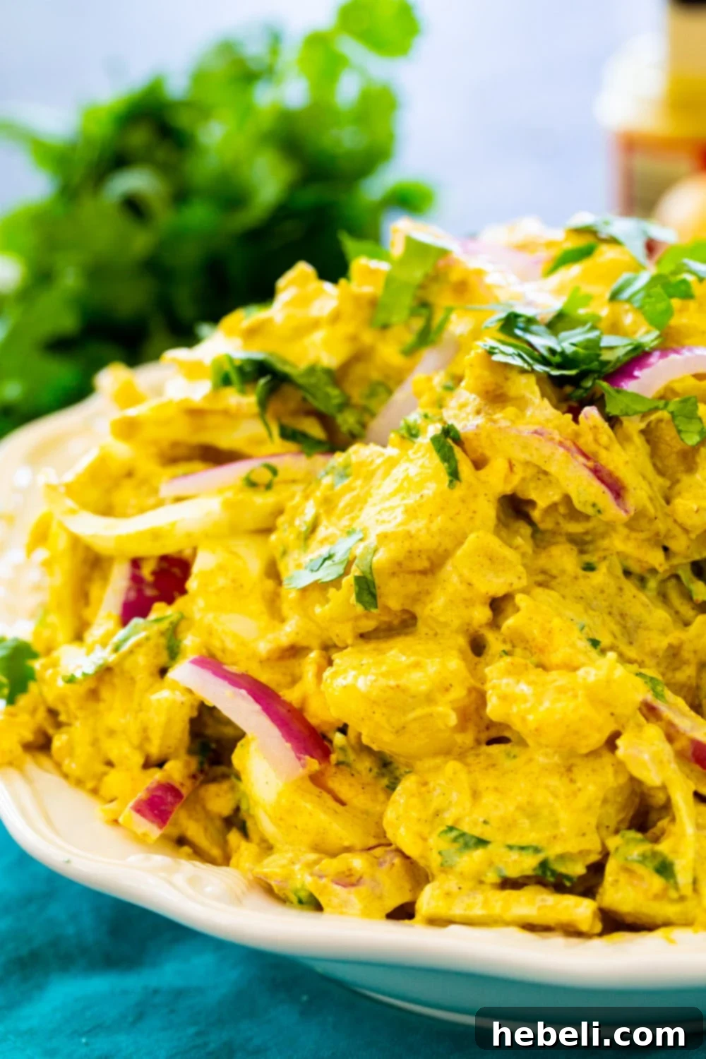 Close-up shot of creamy Curried Potato Salad, highlighting the texture of the potatoes, eggs, and red onion.