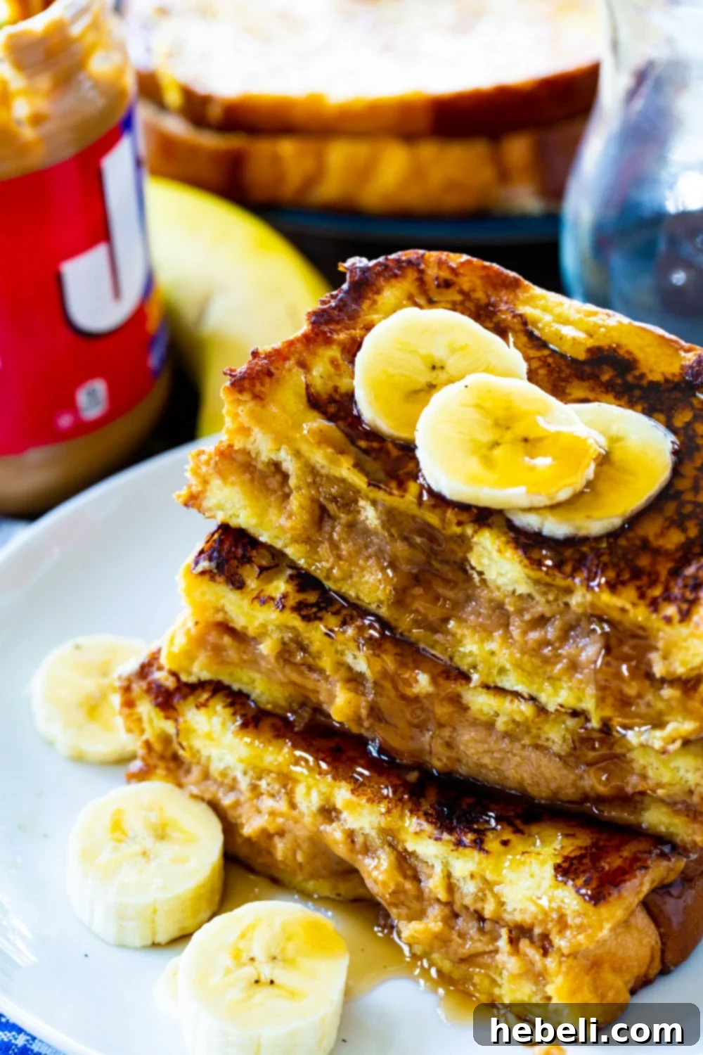 Individual serving of French Toast topped with fresh banana slices and a drizzle of syrup on a white plate.