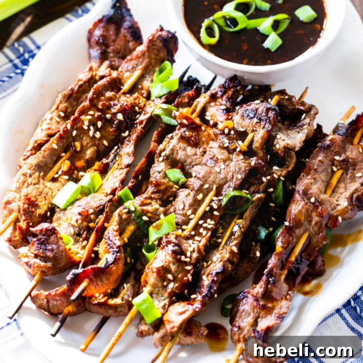 Marinated Steak Skewers with Korean BBQ Sauce on a white serving plate, garnished with sesame seeds and green onions.
