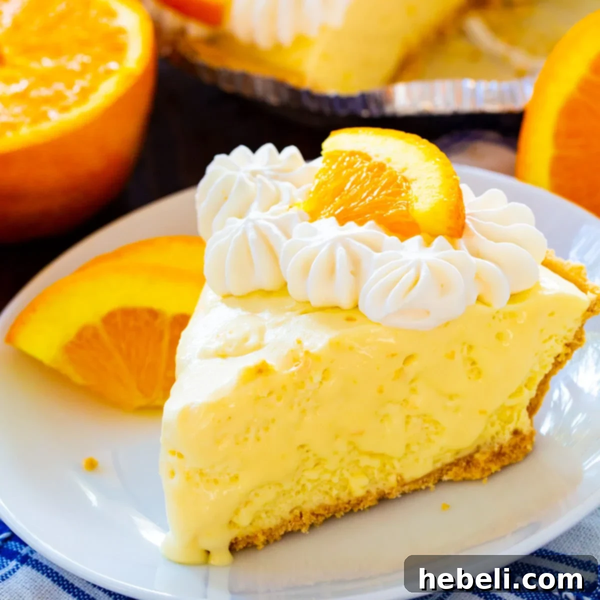 A beautifully sliced piece of Orange Creamsicle Pie, showcasing its creamy texture and vibrant orange color, garnished with whipped cream and an orange slice on a white plate.