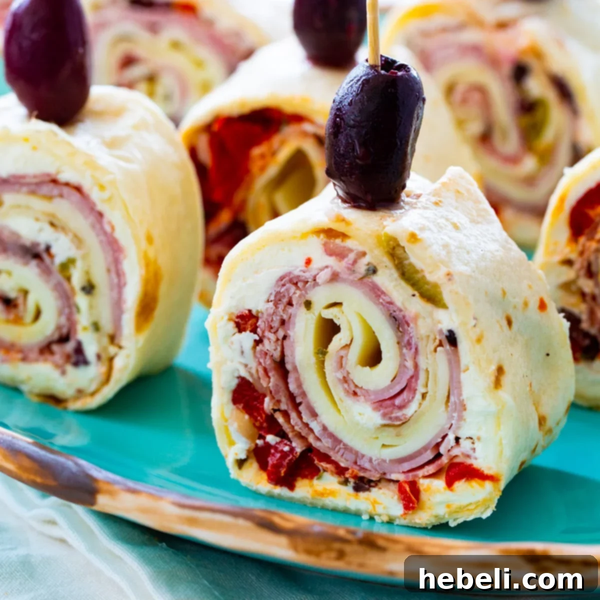 Muffaletta Pinwheels topped with black olives on a plate, ready to be served as an appetizer.